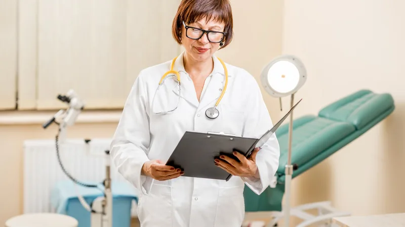 Ginecologista analisando documentos financeiros com um notebook e estetoscópio, representando a gestão de CNPJ e finanças médicas.