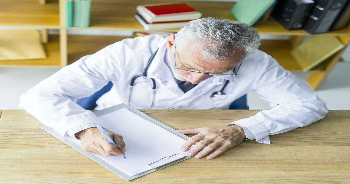 Médico analisando documentos fiscais e um computador, representando a complexidade da DMED para especialistas da saúde.