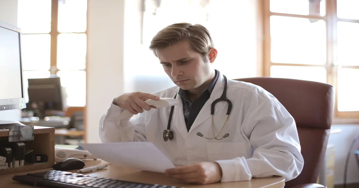 Médico PJ analisando documentos fiscais com calculadora e computador, simbolizando a retenção de IRRF e planejamento tributário.