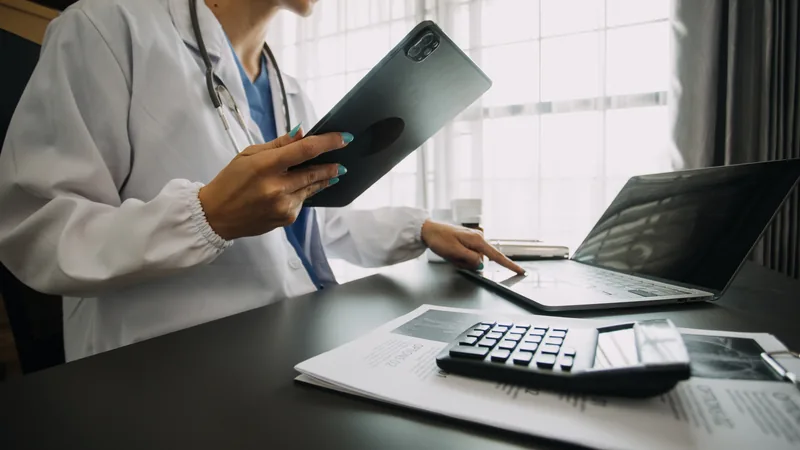 Médico analisando gráficos de simulação tributária em um tablet, com símbolos de dinheiro e impostos ao fundo, representando otimização fiscal para PJ.